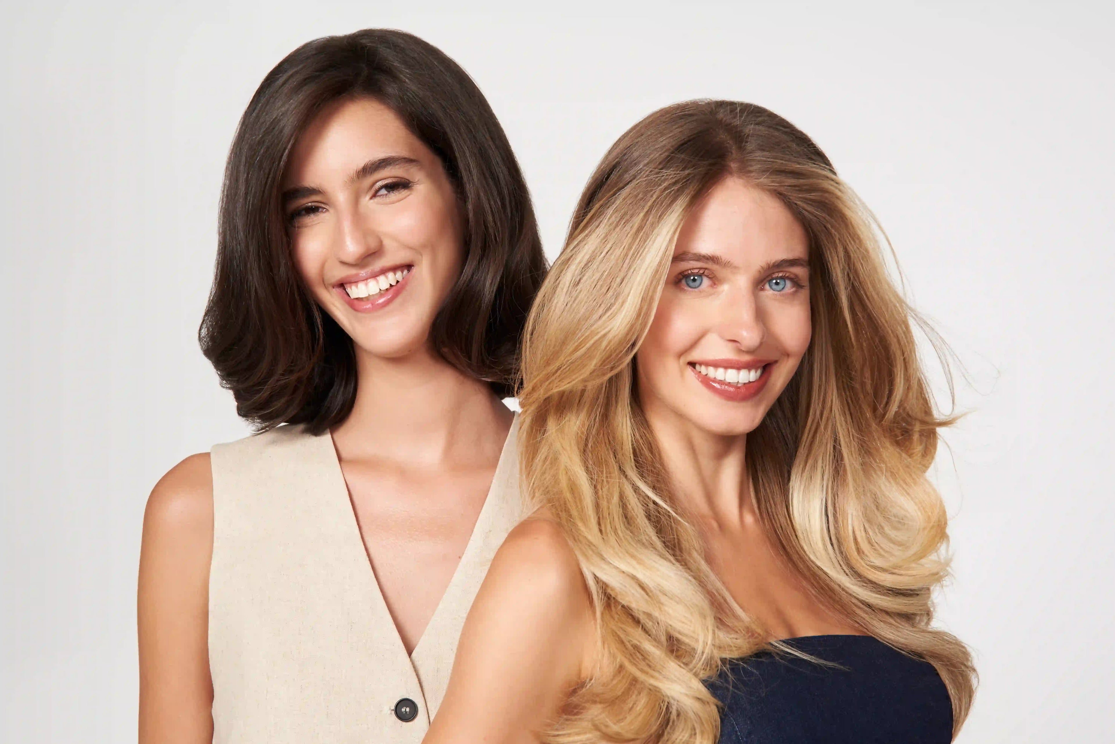 Twee modellen met gezond, glanzend haar in een lifestyle haarverzorgingsbeeld. De afbeelding toont een blonde en een brunette look en is ideaal om de professionele en verzorgende uitstraling van het haarverzorgingsmerk te versterken.